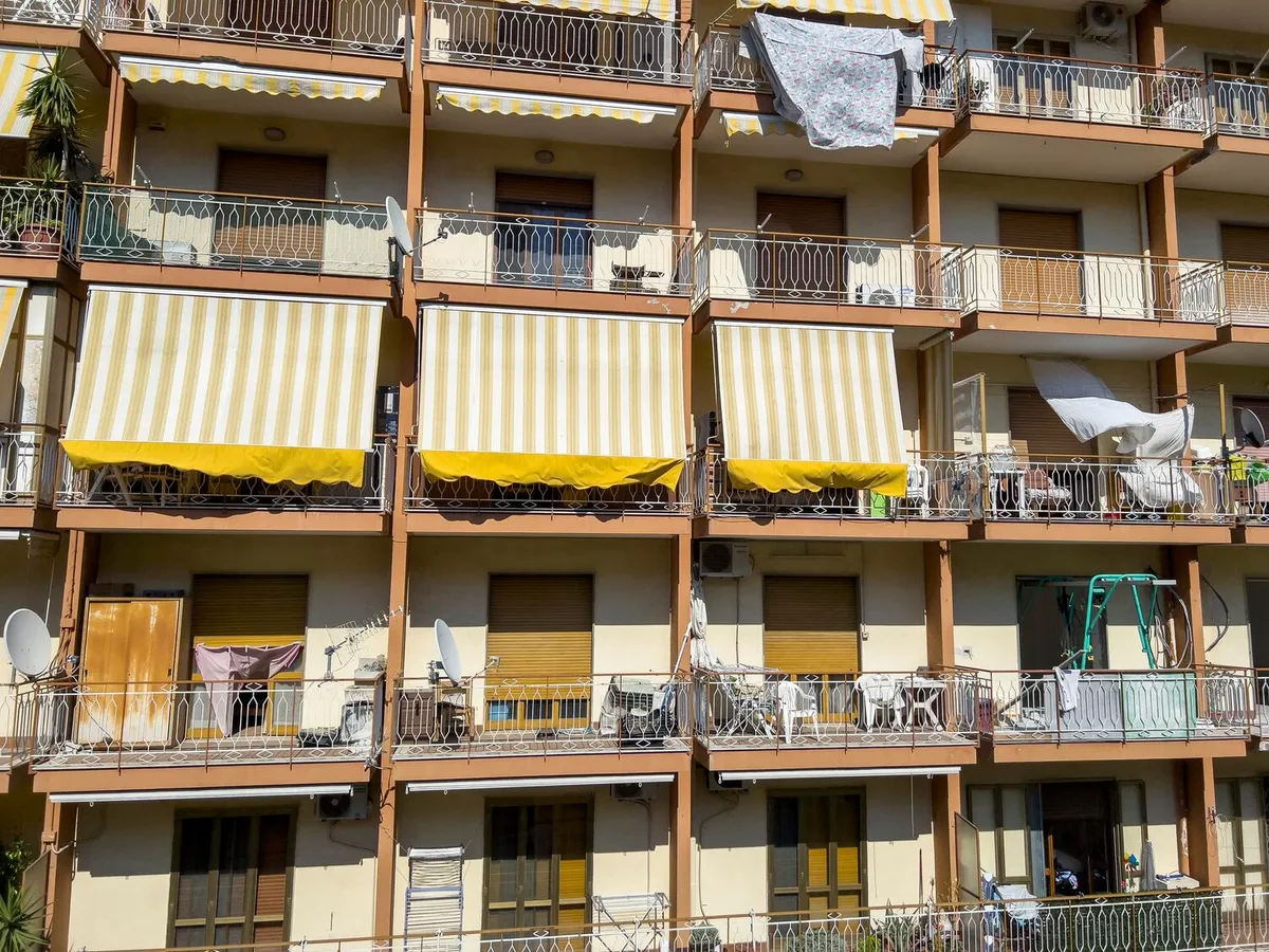 Façade d'immeuble avec stores bannes rayés jaune et blanc déployés au-dessus des balcons et volets roulants à mi-hauteur